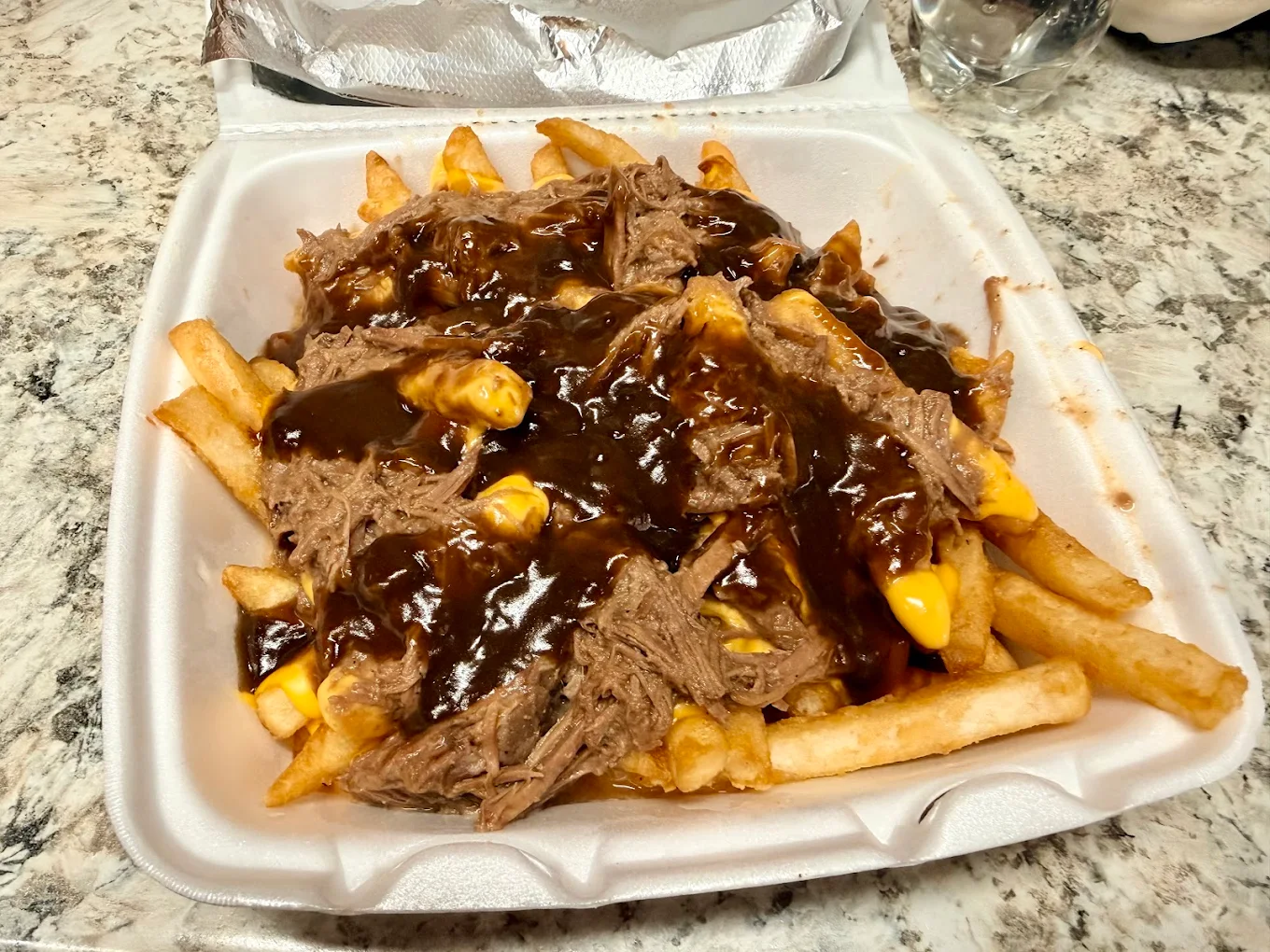 Takeout plate with roast beef, gravy, and french fries in a foam container.